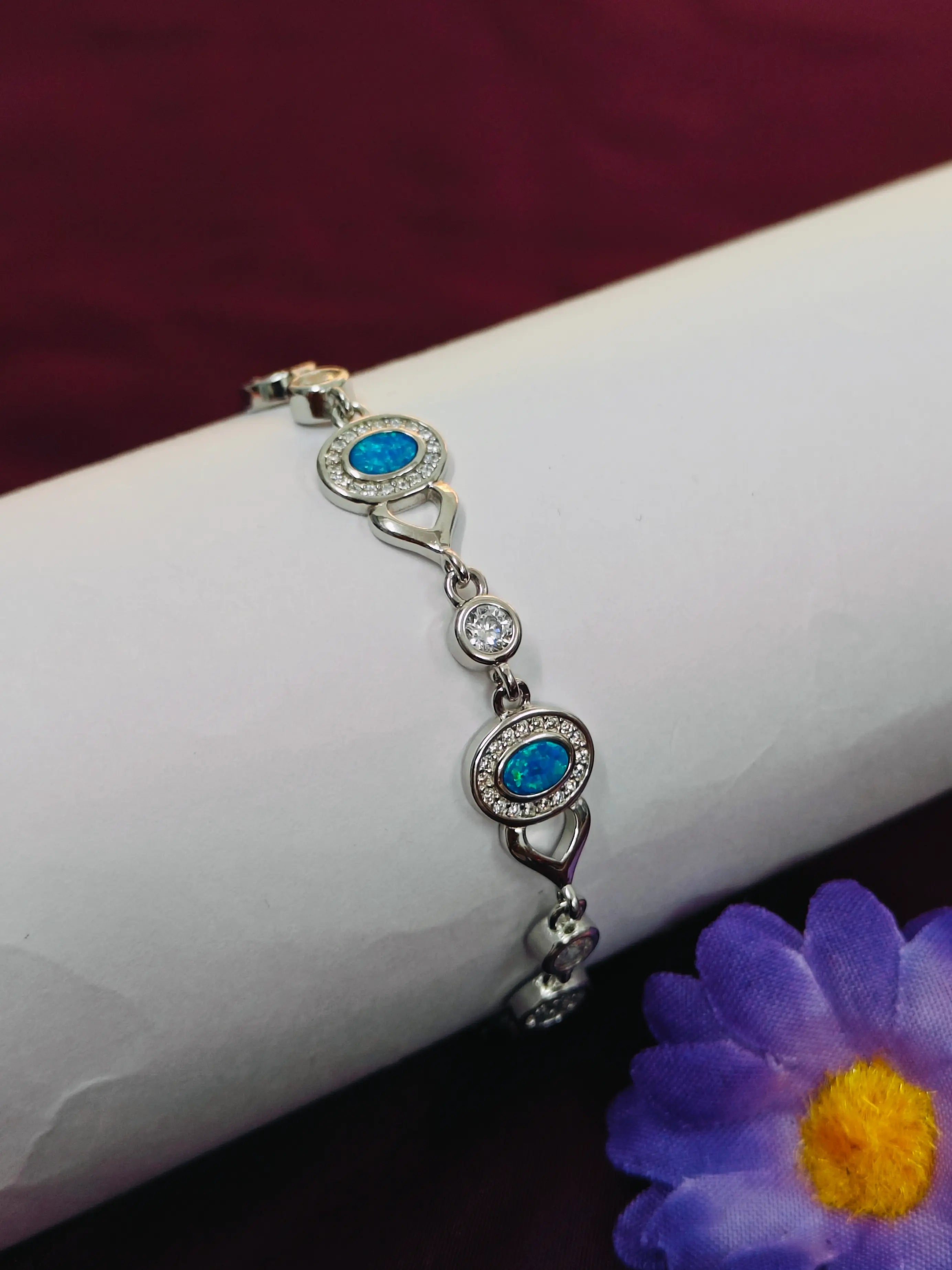 Silver bracelet with blue gemstones on a white arm with a purple flower in the background